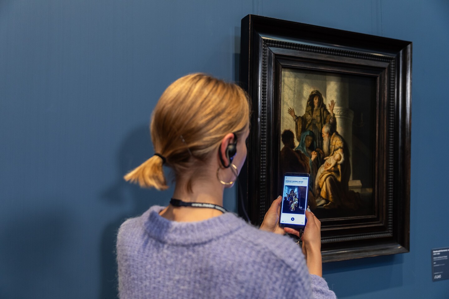 Eine Frau mit Handy und Kopfhörern vor dem Gemälde von Rembrandt Harmensz. van Rijn (1606–1669)