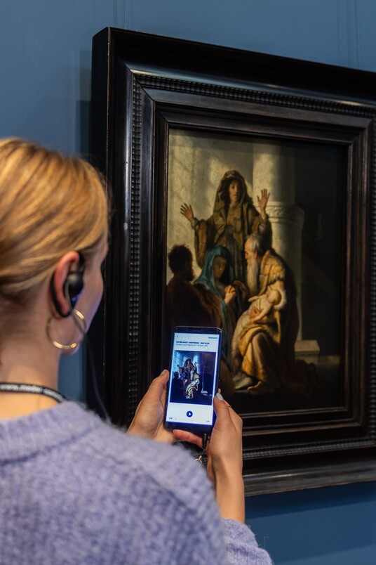 Eine Frau mit Handy und Kopfhörern vor dem Gemälde von Rembrandt Harmensz. van Rijn (1606–1669)